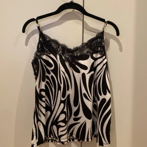 Svartvit mönstrad linnetopp från Amisu - Snygg svartvit linnetopp från Amisu med ett abstrakt mönster. Toppen har spetsdetaljer vid halsringningen och tunna axelband. Perfekt för en stilren look. Har bara använt den 1 gång. 