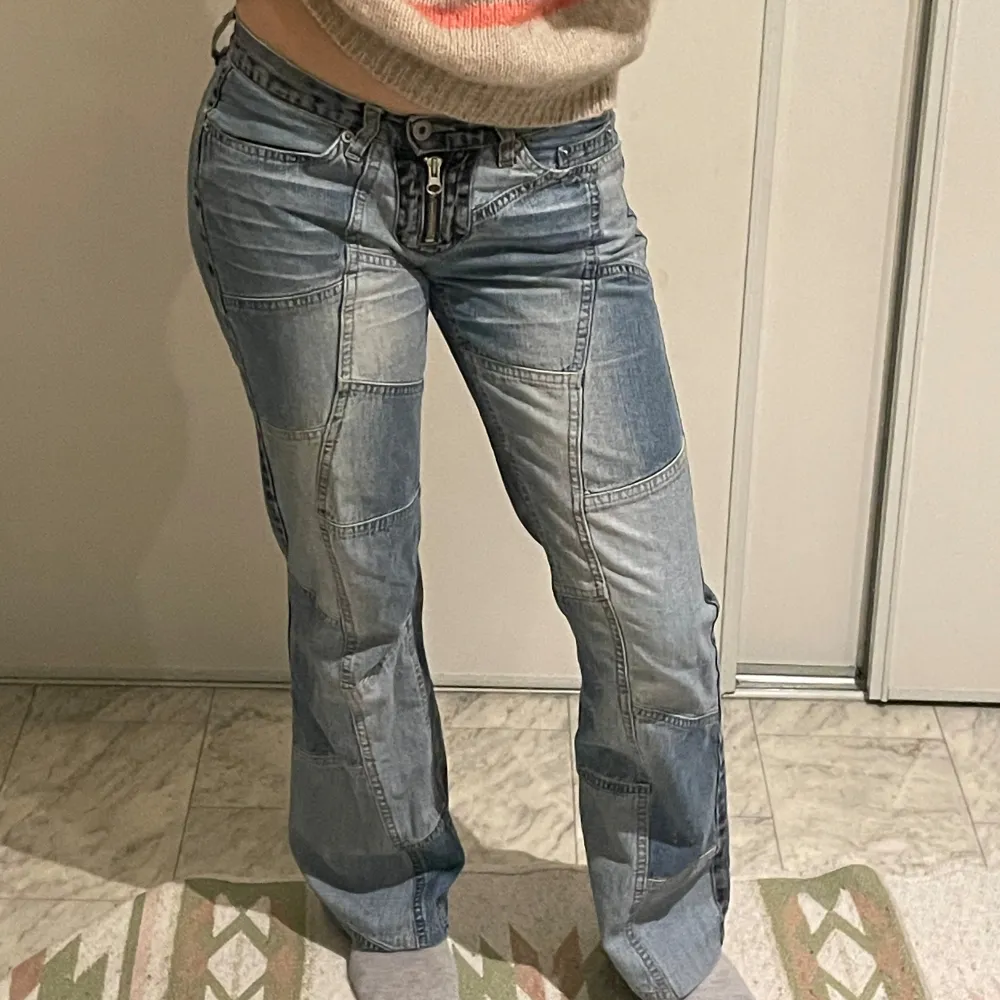 Snygga blå jeans med unik patchwork-design och bootcut-stil. De har en låg midja och knappar framtill. Perfekta för en avslappnad look med en twist.. Farkut & Housut.