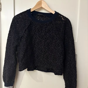 Svart spetsmönstrad tröja från Zara Woman - Säljer en elegant svart spetsmönstrad tröja från Zara Woman. Tröjan har långa ärmar och en ribbad krage samt muddar. Perfekt för att ge en stilfull touch till din outfit.
