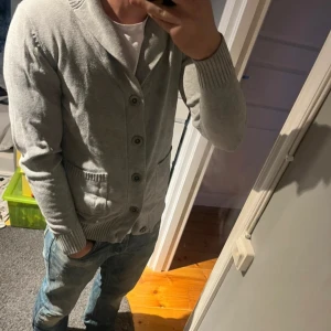 Grå overshirt - Säljer en stilren grå kofta från Selected Jeans. Koftan har knappar framtill och två praktiska fickor. Perfekt för kyligare dagar med sin mjuka och bekväma passform.