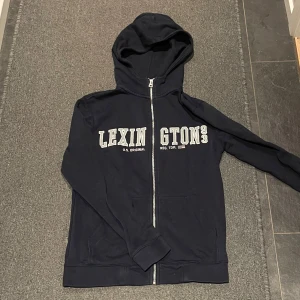 Mörkblå hoodie från Lexington - Säljer en super snygg mörkblå hoodie från Lexington med dragkedja och tryck framtill. 