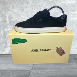 Axel arigato skor herr  - Snygga svarta sneakers från Axel Arigato med stilren design och vit sula. Skorna har snörning och är perfekta för en modern look. Levereras i originalförpackning. [ Budes kontroll]