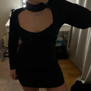 Svart klänning med öppen byst - Snygg svart klänning från Gina Tricot med en unik öppen byst och hög krage. Klänningen är långärmad och har en tight passform som framhäver figuren. Perfekt för en kväll ute eller en speciell tillställning.(passar  xs-m)