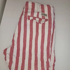 Randiga shorts från Made in the Shade - Snygga randiga shorts i rött och vitt från Made in the Shade. Perfekta för en avslappnad stil under varma dagar. Garderobsrensning så kika gärna på övriga auktioner. 