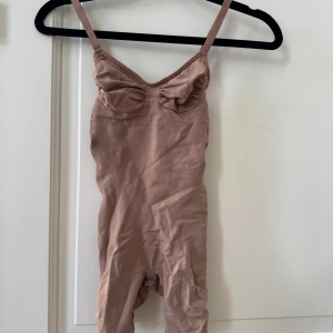 Beige bodysuit från Skims - Säljer Skims shapewear seamless sculpt beige bodysuit. Perfekt att ha under kläder, för att forma kroppen. Men passar även att ha som en topp! Köpt för 1100kr, använd en gång