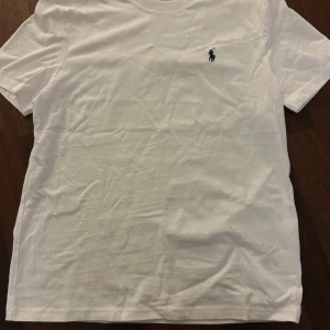 Vit t-shirt från Polo Ralph Lauren - Säljer en vit t-shirt från Polo Ralph Lauren med den ikoniska loggan broderad i blått. Tillverkad i mjuk bomull. Storlek M.