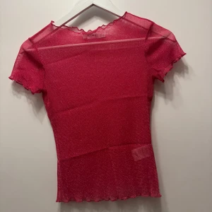 Rosa glittrig mesh-topp - Rosa glittrig mesh-topp från NAKD. Toppen har korta ärmar och en vågig kant vid halsen och nederkanten. Perfekt för att lägga till lite glitter i din outfit 💗
