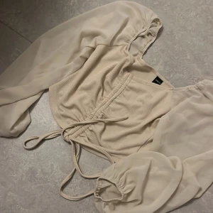 Beige croppad blus från shein - Säljer en stilren beige croppad blus från H&M med långa, transparenta ärmar och knytning i midjan. Perfekt för en trendig look.