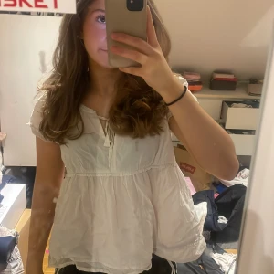 Vit blus - Säljer en söt vit blus med korta ärmar och knytband framtill. Blusen har en lös passform och ett broderat blommönster vid halsen. Perfekt för en avslappnad stil eller till fest! Ignorera att den är skrynklig, jag stryker innan den postas ❤️