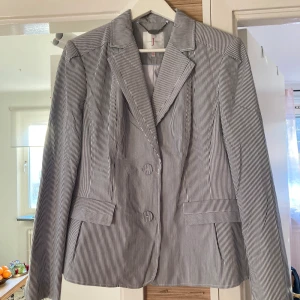 Randig kavaj från Jasper Conran - Snygg randig kavaj från Jasper Conran i blått och vitt. Kavajen har en klassisk krage och knäppning framtill med två knappar. Perfekt för en stilren look.