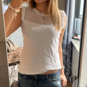 Vit topp med spetsdetaljer - Säljer en söt vit topp med superfina spetsdetaljer på övre delen! Köpt secondhand men aldrig använd