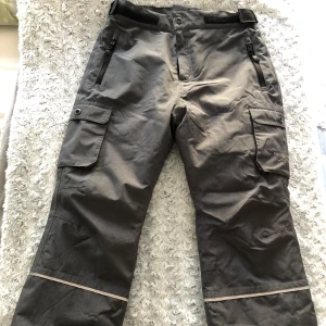 Grå varma överdragsbyxor från Swedemount - Säljer ett par grå överdragsbyxor från Swedemount med praktiska fickor och knappar. Byxorna har en justerbar midja och dragkedjor vid fickorna. Perfekta för utomhusaktiviteter och äventyr.Finns hängslen till med. Använda endast 1 gång! 