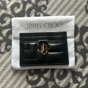 Svart korthållare från Jimmy Choo - PERFEKT VALENTINES PRESENT! Snyggt svart kortfodral från Jimmy Choo i skinn med quiltad design. Fodralet har en elegant gulddetalj med JC-logotypen på framsidan. Perfekt för att hålla dina kort stilfullt organiserade.