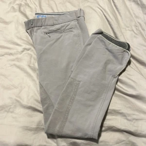 Beige ridbyxor från CRW - Snygga beige ridbyxor från CRW, perfekta för ridning. De har en klassisk design med dragkedja och knapp framtill. Byxorna är tillverkade i ett slitstarkt material som ger bra komfort och rörelsefrihet.