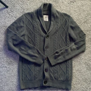 Mörkgrå kofta med knappar - Säljer en stilren mörkgrå kofta med knappar och kabelstickat mönster. Den har långa ärmar och en klassisk krage. Perfekt för kyligare dagar. Ny pris runt 1000kr mitt pris 499! Priset är ej hugget i sten så bara komma med prisförslag. Skick 9,5/10 nästan helt ny. Skriv för fler frågor eller bilder. Modellen är 185