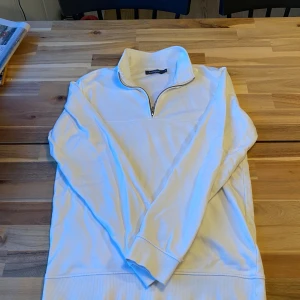 Vit tröja med dragkedja från Dressmann - Säljer en stilren vit tröja från Dressmann i storlek M. Tröjan har en dragkedja vid halsen och är tillverkad av bomull och polyester. Perfekt för en avslappnad stil.