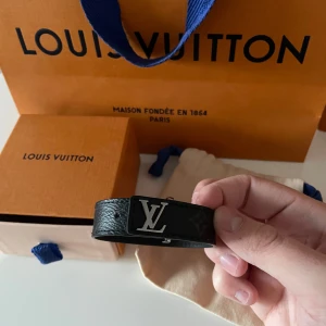 LV armband - Snyggt svart Armband från Louis Vuitton med en elegant LV-logotyp i silver. Armbandet har en stilren design och är perfekt för att ge en lyxig touch till din outfit. Kommer i originalförpackning med påse, box o kvitto