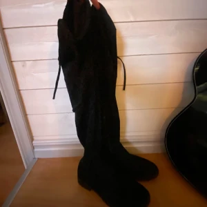 Svarta höga stövlar - Snygga svarta stövlar i mocka som går över knäna, vid knäna finns det snöra som man kan knyta och spänna åt. Perfekta för en stilren look och passar bra till både kjol och byxor. 