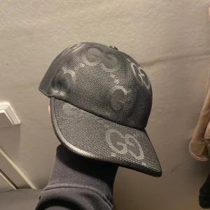 Svart keps från Gucci - Snygg svart keps från Gucci med det ikoniska GG-mönstret. Kepsen har en klassisk design med böjd skärm och justerbar passform. Perfekt för att ge en lyxig touch till din outfit.