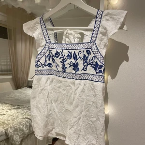 Vit blus - Säljer en vit blus med söta blå broderier på bröstet. Den har en söt knytning i ryggen som ger en extra detalj.💓