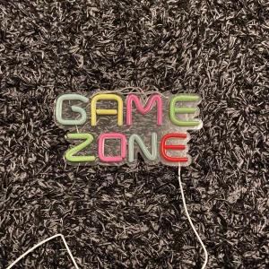 Neonskylt 'Game Zone' - Cool neonskylt med texten 'Game Zone' i flera färger. Perfekt för spelrummet eller som en unik inredningsdetalj. Skylten lyser i blått, grönt, rött och gult och har en strömkabel för enkel anslutning.
