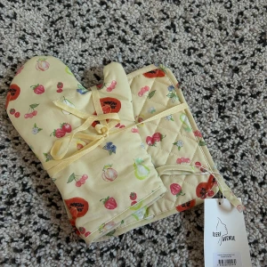 Gula grytvantar med fruktmönster från Djerf Avenue - Säljer ett par söta gula grytvantar med ett färgglatt fruktmönster från Djerf Avenue. Perfekta för att liva upp köket med sina jordgubbar, papayor och körsbär. Grytvantarna har en praktisk ögla för upphängning och kommer med en matchande grytlapp. Ett måste för den stilmedvetna kocken! 🍓🍒