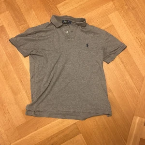 Grå pikétröja från Ralph Lauren - Säljer en stilren grå pikétröja från Ralph Lauren med broderad logga på bröstet. Tröjan har korta ärmar och en klassisk krage med knappar. Perfekt för en avslappnad men ändå snygg look. Pris kan diskuteras skriv för Minsta fråga 