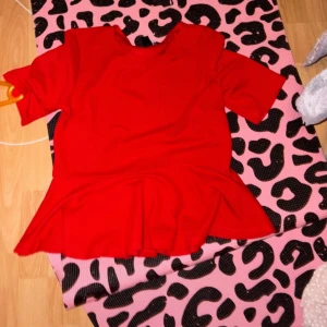 Röd topp med volangdetalj - Snygg röd topp med volangdetalj i nederkant. Perfekt för att lägga till en färgklick i garderoben. Toppen har korta ärmar och en rund halsringning.