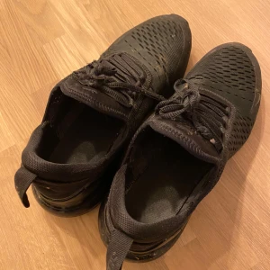 Svarta Nike sneakers - Säljer ett par svarta Nike sneakers med snörning och ventilerande meshmaterial. Skorna har en sportig design och är perfekta för vardaglig användning. De är märkta med Nike-loggan på sidan.