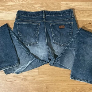 Blå jeans från Wrangler - Säljer ett par klassiska blå jeans från Wrangler. De har en straight passform och ett hål vid frambentet. 