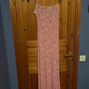 Rosa långklänning från BikBok - Säljer en elegant rosa långklänning från BikBok med ett vackert blommigt mönster. Klänningen har smala axelband och en figurnära passform som framhäver silhuetten. Perfekt för sommaren då den är lite genomskinlig och luftig🤍🌸 har endast använt en gång på skolavslutningen men säljer så jag ej använt sen dess! (Pris går alltid att diskuteras)