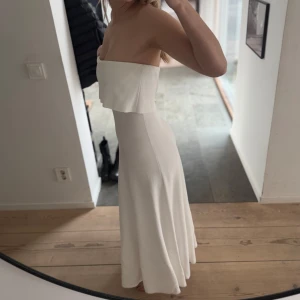 Vacker vit axelbandslös klänning - Säljer min fina vita axelbandslös klänning! Slutsåld på twist and tango. Klänningen har en lång längd och en mjuk, flytande passform som ger en vacker siluett. Perfekt för speciella tillfällen. Använt endast 1 gång på min examen!   Orginalpris 2199 kr