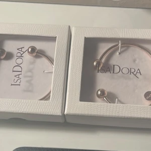 Guldfärgade armband från IsaDora - Två eleganta guldfärgade armband från IsaDora. Armbanden har en minimalistisk design med två kulformade ändar. Perfekta för att lägga till en touch av stil till din outfit.