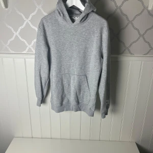 Grå hoodie - Säljer en stilren grå hoodie med känguruficka framtill. Perfekt för en avslappnad look. Den har en klassisk passform och är tillverkad i mjukt material för extra komfort.