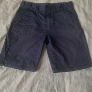 Mörkblå shorts från Tommy Hilfiger - Snygga mörkblå shorts från Tommy Hilfiger med knapp och dragkedja framtill. Klassisk design med två sidofickor och två bakfickor. Perfekta för en stilren look.