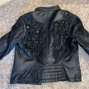 Svart skinnjacka från Culture - Snygg svart skinnjacka från Culture med coola paljettdekorationer på axlar och rygg. Stl M, speciell beställd och köpt för över 3000kr. Mitt pris 899kr men kan diskutera vid smidig affär