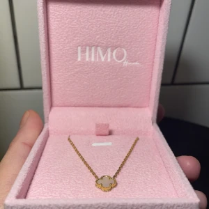 Guldhalsband med fyrklöverberlock från HIMO - Elegant guldhalsband från HIMO med en fyrklöverformad berlock. Berlocken har en vit inläggning som ger en stilren och klassisk look. Perfekt för att lägga till en touch av lyx till din outfit. Samt vattentåligt 