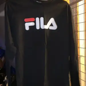Säljer en svart långärmad tröja från FILA med deras ikoniska logga i vitt och rött på bröstet. Perfekt för en casual look. Tröjan är i storlek XS och har en klassisk rund halsringning. 