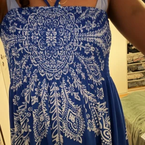 Blå klänning med vitt mönster - Säljer en blå klänning med ett vackert vitt mönster. Klänningen har en smockad överdel och är ärmlös med halterneckband. Perfekt för stranden, kan användas som både klänning och kjol! Köpt på en Fransk marknad för 240 svenska kronor! Aldrig använder den tyvärr. Färgen liknar kungsblå/marknblå. 