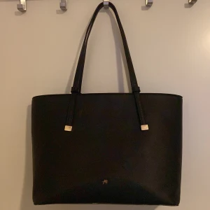 Svart axelväska från Anna Field - Snygg svart axelväska från Anna Field med stilrena linjer och guldfärgade detaljer. Perfekt för att bära med sig allt man behöver. Väskan har ingen dragkedja men har en magnet.