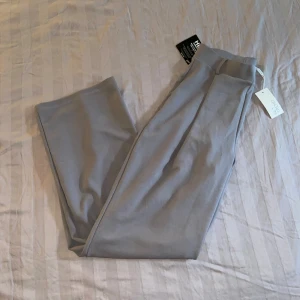 Grå byxor från Hey - Säljer ett par oanvända snygga grå byxor från NLY trend med alla lappar kvar. De är högmidjade och har en loose passform med vida ben. Perfekta för både vardag och fest! Har legat i mitt förråd så kan lukta (eftersom jag ej kan tvätta de med lappar)