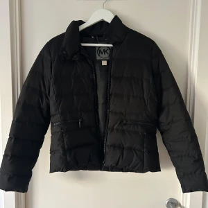 Svart pufferjacka från Michael Kors - Säljer en snygg svart pufferjacka från Michael Kors i storlek M. Jackan har en dragkedja framtill och två praktiska fickor med dragkedjor. Perfekt för kyliga dagar och ger en stilren look. Passar både till vardags och lite finare tillfällen.