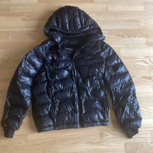 Svart pufferjacka från Peak Performance - Säljer en snygg svart pufferjacka från Peak Performance. Den är perfekt för kalla dagar med sin quiltade design och varma huva. Nypris 2500 kr men den är använd. Jackan har små defekter men märks knappt: Se 2 sista bilder