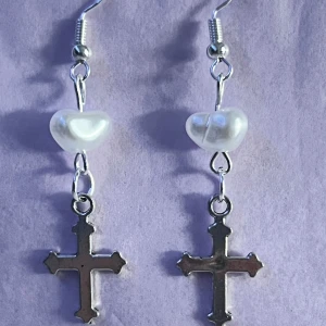 Örhängen med kors och pärlhjärtan - Snygga örhängen med ett kors i silverfärg och ett pärlhjärta ovanför. Perfekta för att ge en stilren touch till din outfit. De är både eleganta och lite edgy, vilket gör dem perfekta för både vardag och fest. I sterling silver✝️🩶