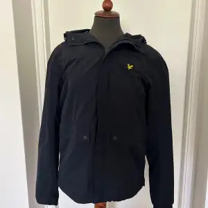 Säljer en stilren mörkblå windbreaker/jacka med huva och dragkedja. Den har en gul Lyle&scott logga på bröstet. Perfekt för höst och vår! Nyskick