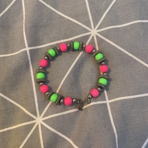Färgglatt armband med pärlor - Säljer ett supercoolt armband med neonrosa och gröna pärlor. Det har också små silverfärgade detaljer som ger en extra touch. Perfekt för att liva upp vilken outfit som helst! Passar både till vardags och fest. 🥳