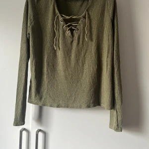 Olivgrön ribbad tröja från Divided - Säljer en olivgrön ribbad tröja från Divided i storlek L. Den har en snygg snörning framtill och långa ärmar. Perfekt för höst och vår när du vill ha något bekvämt men ändå stilrent. Passar både till vardags och lite mer uppklädda tillfällen. 🧶🍂