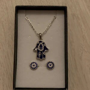Halsband & Örhängen - matchande silvrigt halsband och örhängen  med Hamsa (Fatimas hand) och Nazar (evil eye).  aldrig använda, helt nya.  present box medföljer.  kontakta mig för fler bilder eller frågor 🩵