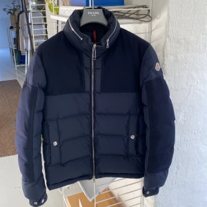Moncler Vinterjacka - Navy dunjacka från Moncler.  Jättebra skick. Sparsamt använd. Enda flaw är som ena bilden visar att ena huvudet på blixtlås dragaren har flugit av. Går utmärkt i övrigt att dra och stänga. Nypris 12.000 kr. Strl 2 men sitter som en M-L. Kort modell. 