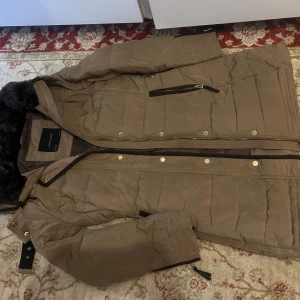 Zara winter coat, Brown, size(medium) - A warm winter jacket with a removable fur collar. The jacket has a zipper and buttons at the front, as well as two pockets with zippers on the sides.  The jacket is in a dark brown color.